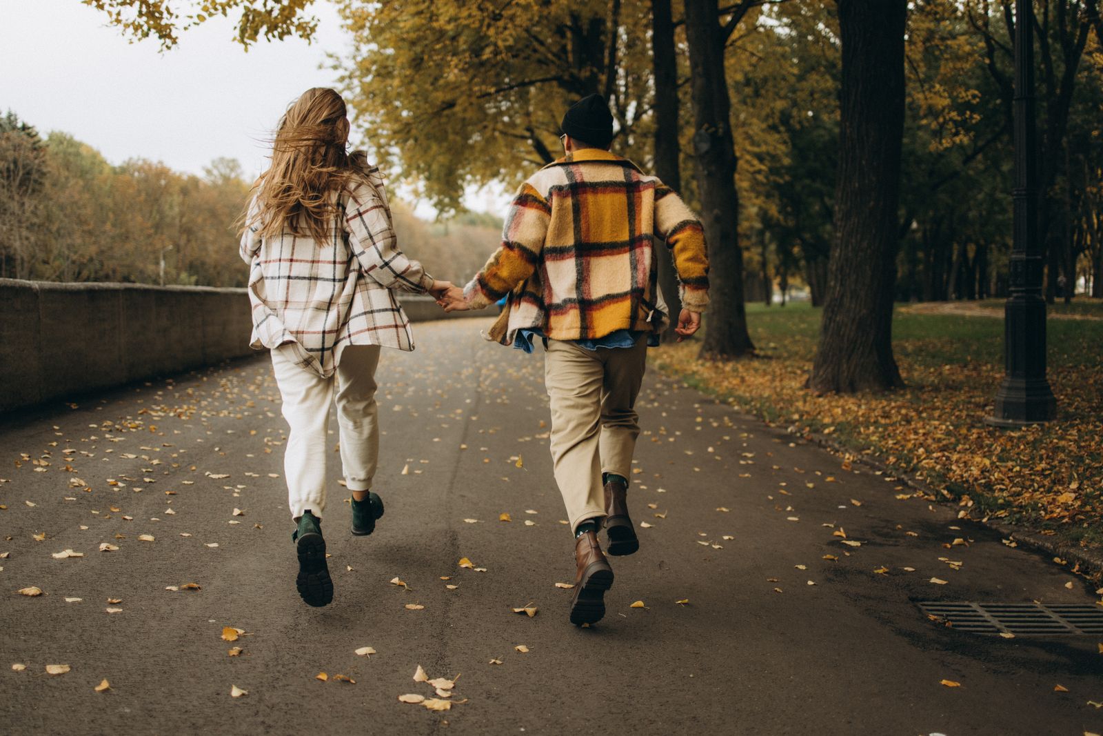 Un couple court main dans la main dans une rue bordée d’arbres en automne